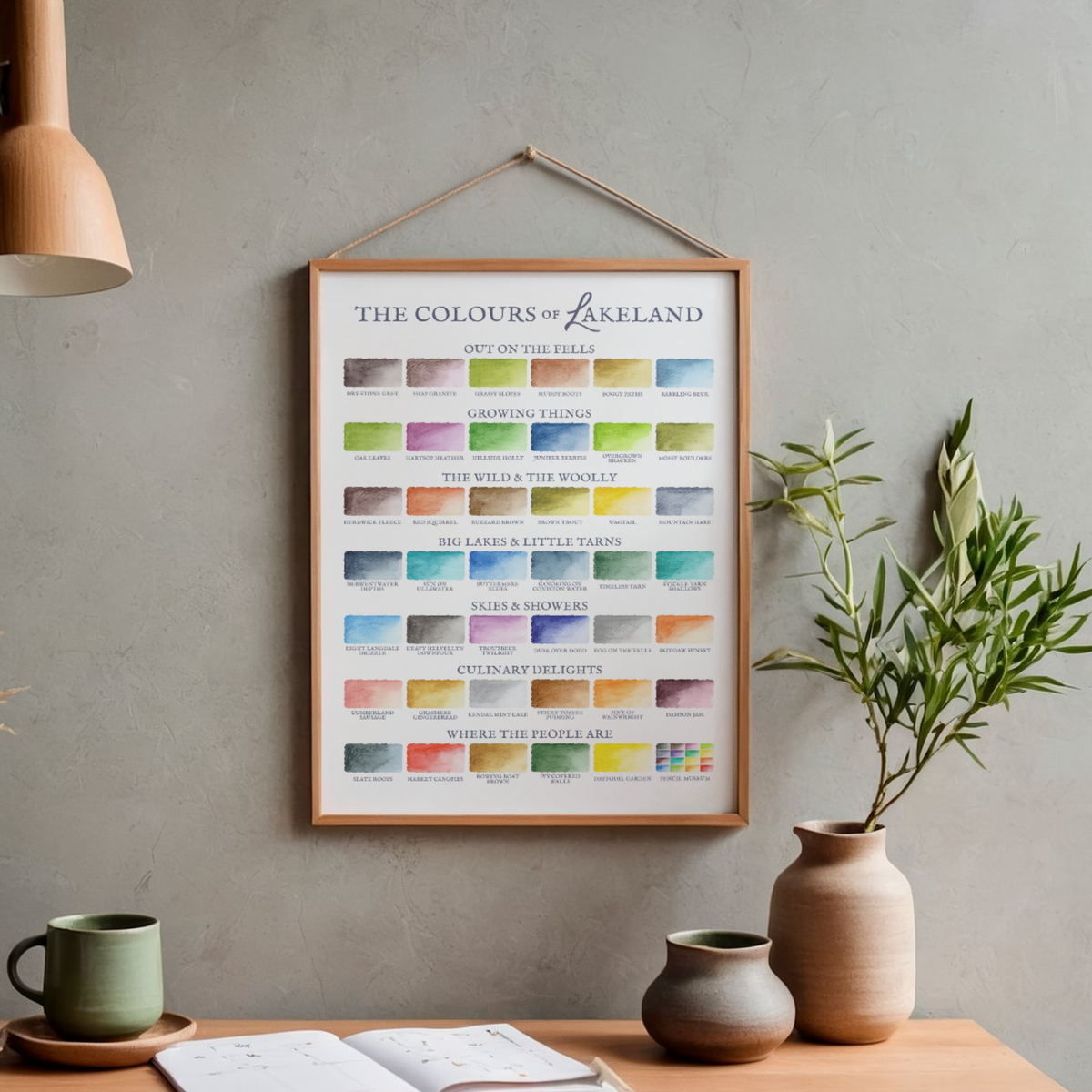 Framed artwork titled 'The Colours of Lakeland' on a wall above a wooden table with decor items.