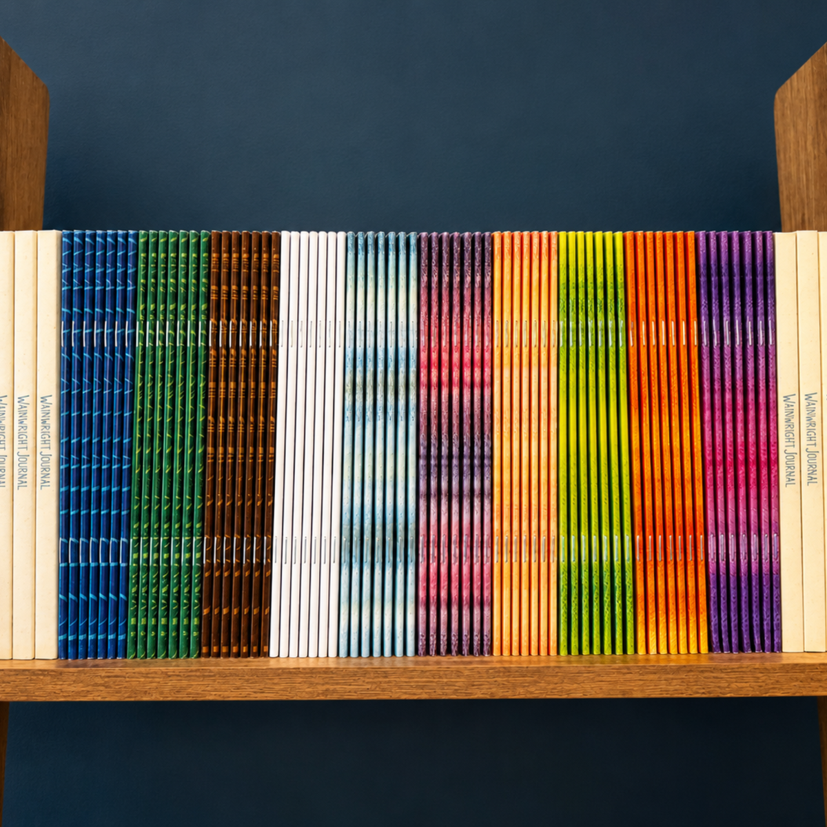A row of colourful notebooks with spines displayed on a wooden shelf against a dark blue background.